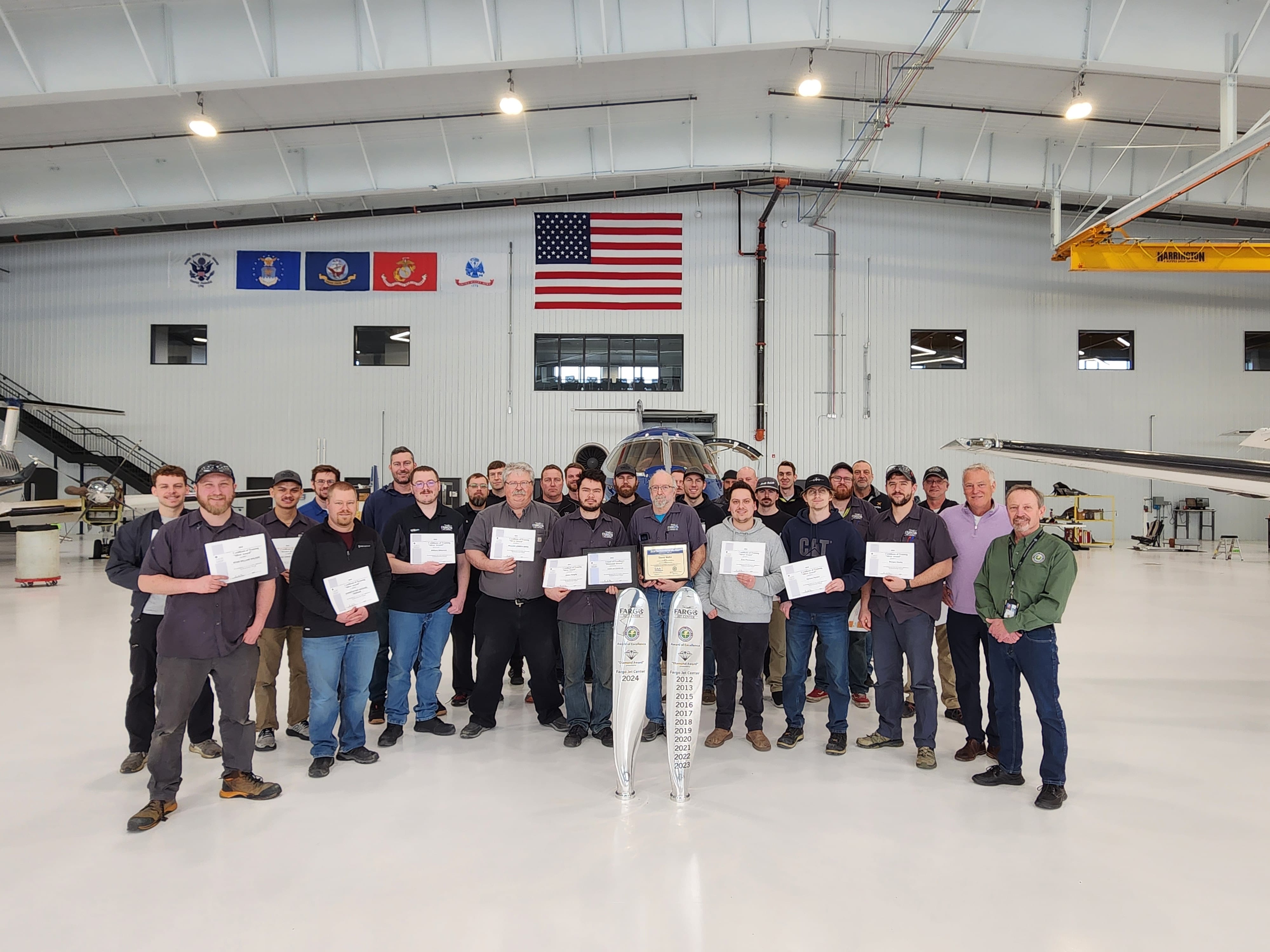 Fargo Jet Center Maintenance Team stands in hangar in front of aircraft, holding award certificates.